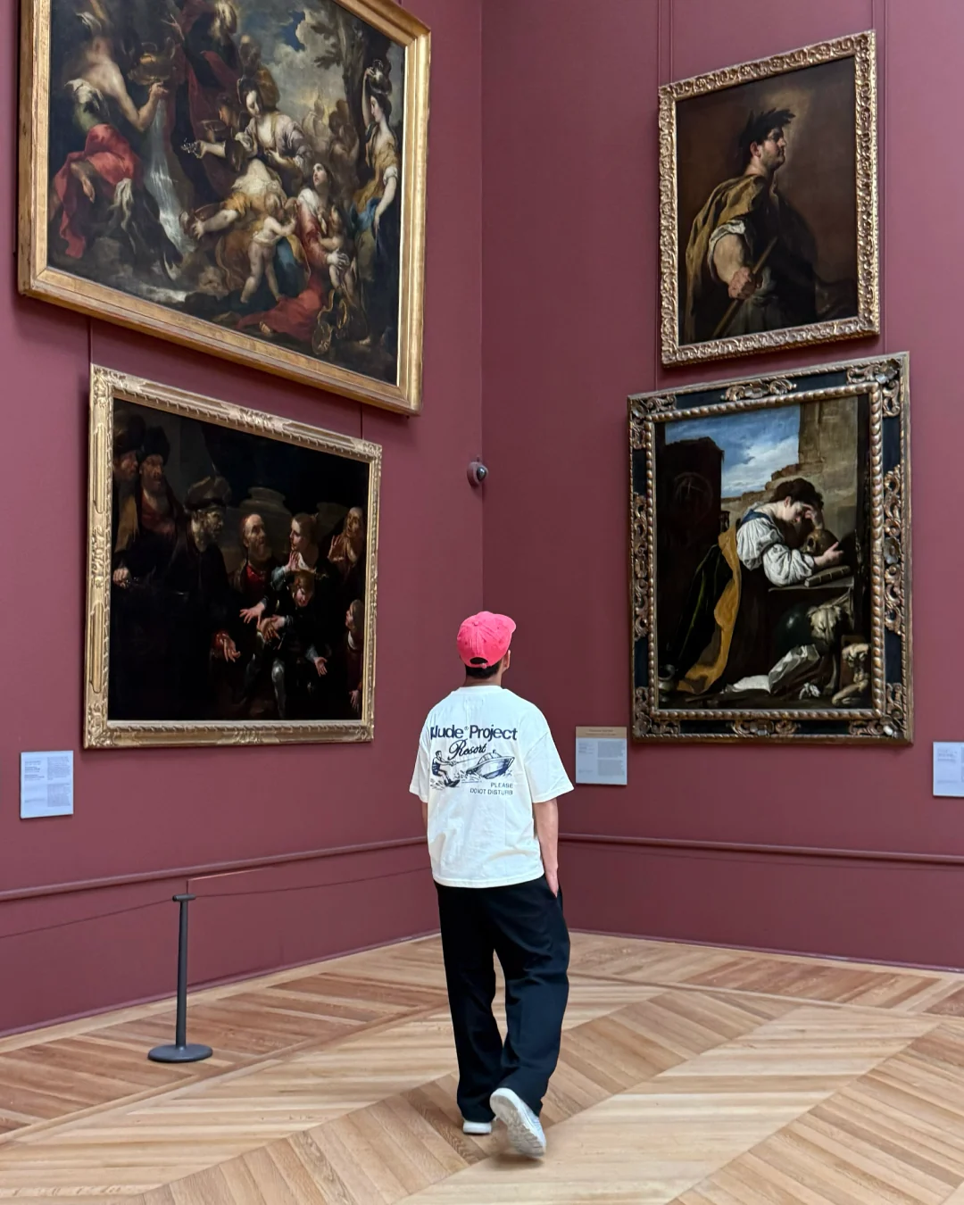 Cristian de espaldas observando pinturas clásicas en un museo de paredes rojas